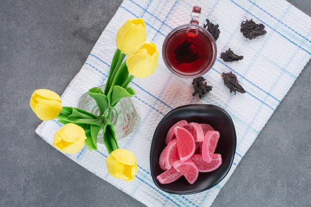 A glass vase of flowers with cup of tea and marmalade.