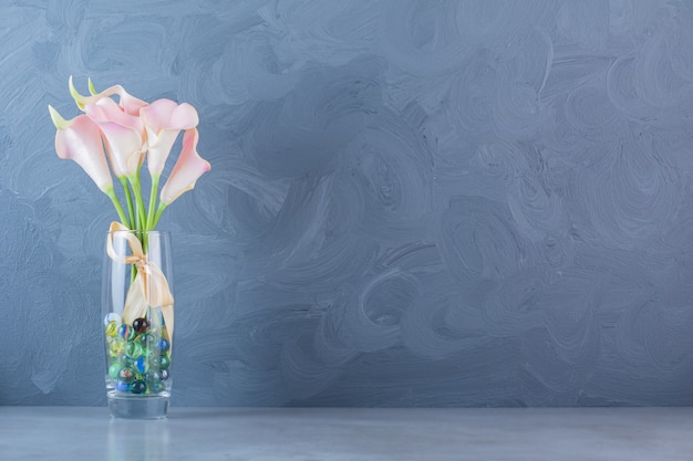 A glass vase of pink beautiful flowers with bow and colorful balls .