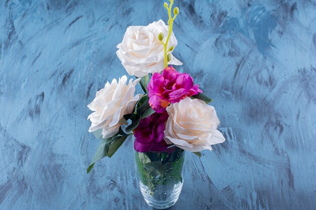 Glass vase of white rose and purple flowers on blue.