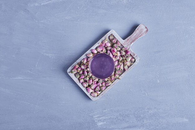 A glass of violet juice with flower blossoms in a wooden platter, top view.