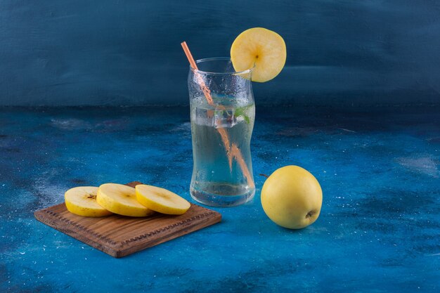 Glass of water and sliced apple placed on marble table.