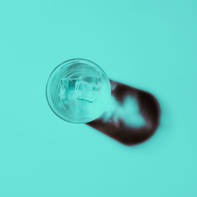 Glass of water with ice cubes on colored background