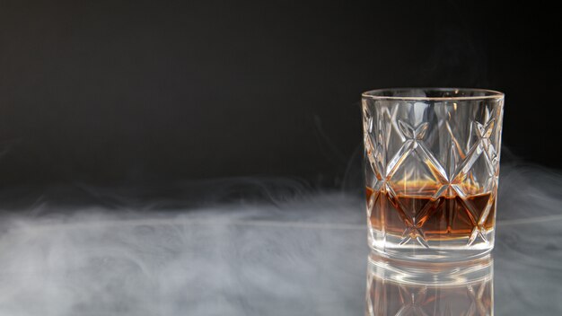 黒の背景に煙に囲まれたテーブルにウイスキーのグラス