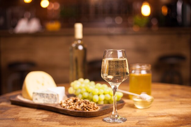 Glass of white wine ,cheese and grapes on old wooden table. Delicious grapes. Fine beverage. Jar of honey.