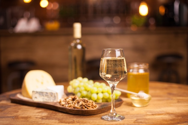 Стакан белого вина, сыра и винограда на старом деревянном столе. Вкусный виноград. Прекрасный напиток. Баночка меда.