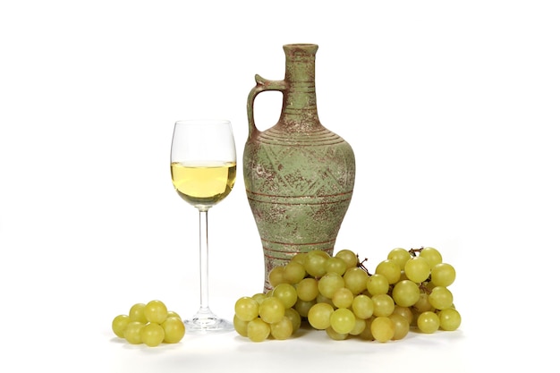 Бокал белого вина рядом с винным кувшином с зеленым виноградом на белом