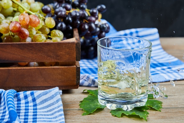 A glass of white wine on wooden table with grapes.