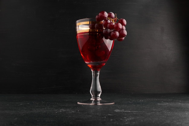 Un bicchiere di vino con un grappolo d'uva sulla superficie nera.