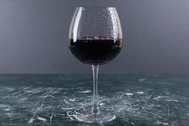 Glass of wine with ice on blue table.