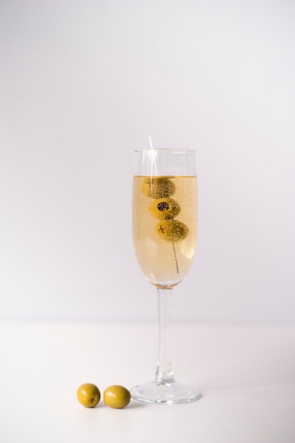Glass with alcohol and olives over white backdrop