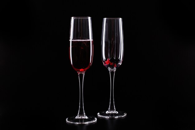 Glass with berries and red champagne alcohol cocktail stands on black background