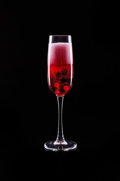 Стекло с ягодами и красное шампанское спиртное коктейль стоит на черном фоне