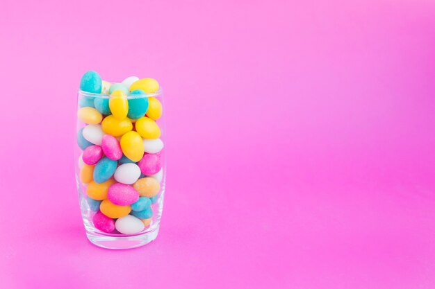 Glass with candies on pink background