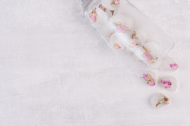 A glass with ice and small roses on white surface