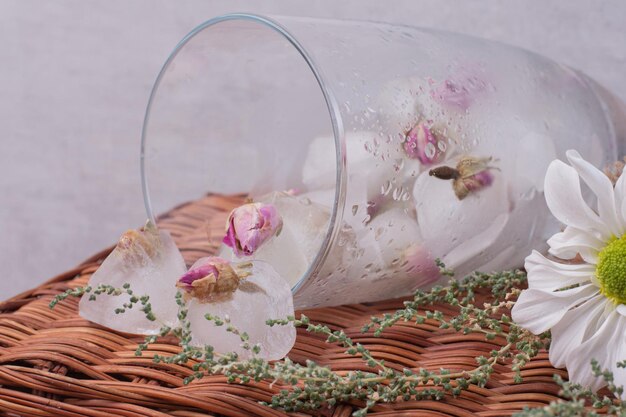 A glass with tiny roses in ice on white table.
