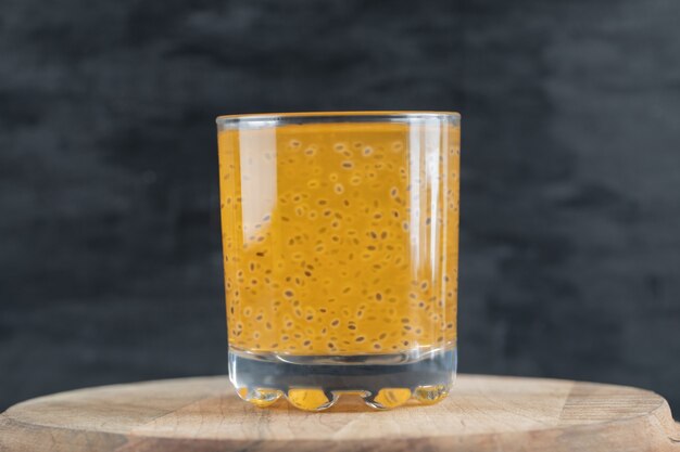 Free photo a glass of yellow orange juice on black on a piece of wooden board