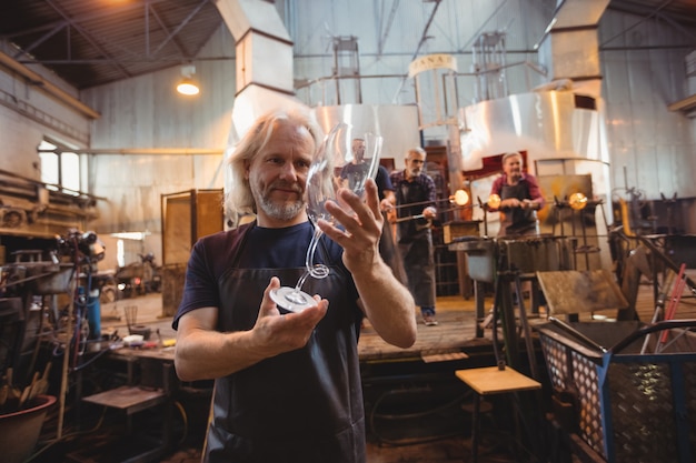 Glassblower examining glassware while colleagues working