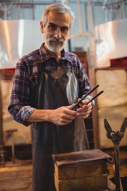 Free photo glassblower holding tongs at glassblowing factory