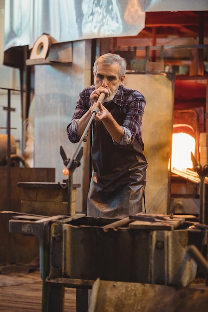 Free photo glassblower shaping a glass on the blowpipe