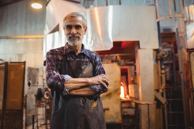 Glassblower standing with arms crossed at glassblowing factory