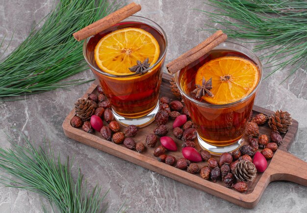 Glasses of black tea with lemon slices on wooden cutting board.