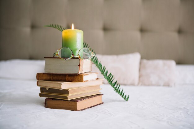 Glasses on books near candle and fern