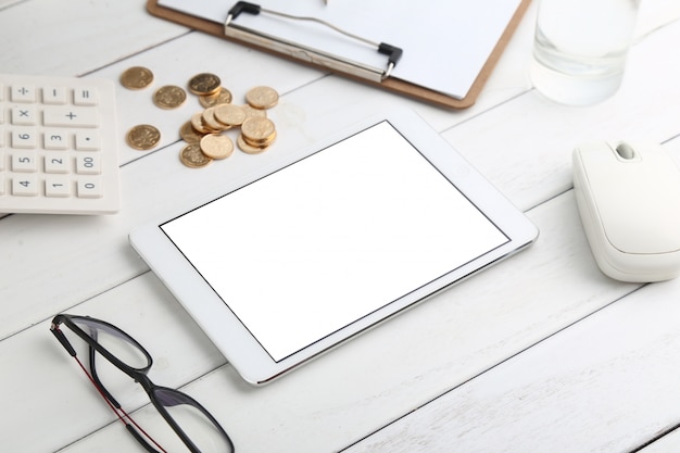 glasses, calculator,coins and tablet on white neat desk