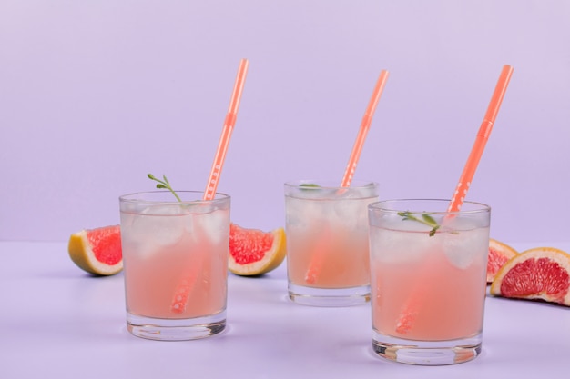 Glasses of cocktail with drinking straws and grapefruits slices on purple background