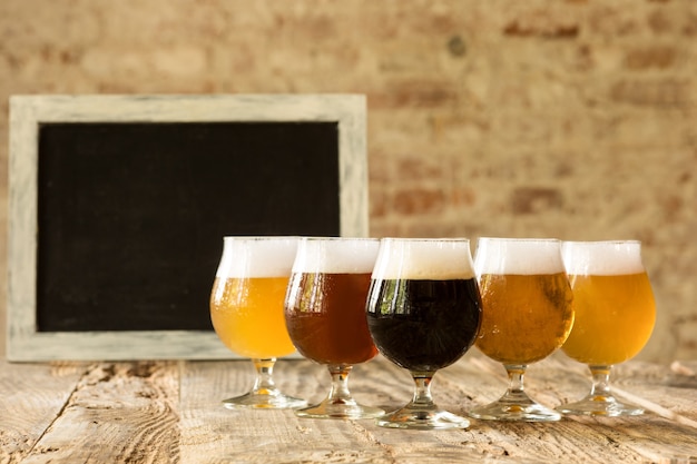 Free photo glasses of different kinds of dark and light beer on wooden table in line