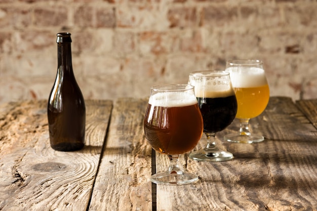 Glasses of different kinds of dark and light beer on wooden table in line