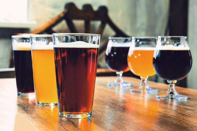 Glasses of different kinds of dark and light beer on wooden table in line