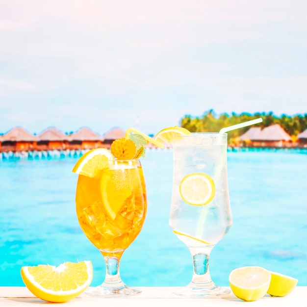 Glasses of juicy lemon orange drinks with straw and sliced citruses
