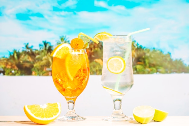 Glasses of juicy orange lemon drinks with straw and sliced citruses