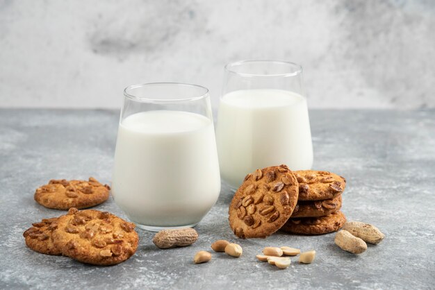 Glasses of milk and homemade cookies with organic peanuts on marble table. 