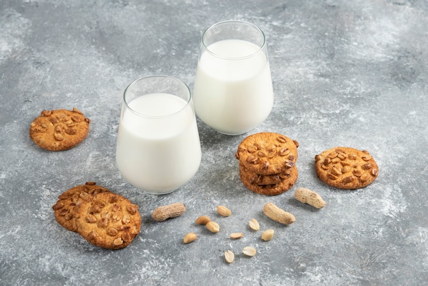 Glasses of milk and homemade cookies with organic peanuts on marble table. 