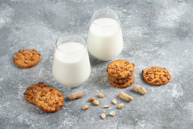 Glasses of milk and homemade cookies with organic peanuts on marble table. 