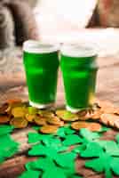 Бесплатное фото Стаканы зеленого напитка возле кучи монет и трилистников из бумаги
