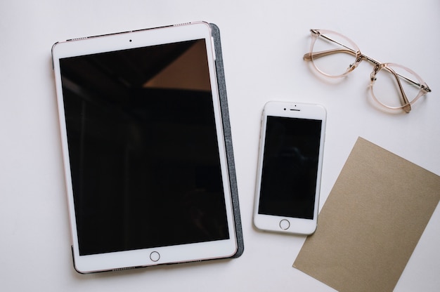 Glasses and paper near tablet and smartphone