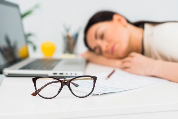 Glasses of sleeping woman on table in office