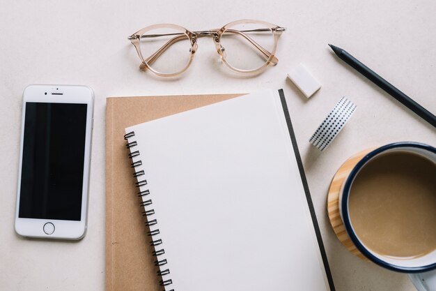 Glasses and smartphone near notebook and coffee