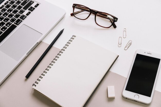 Glasses and stationery between smartphone and laptop