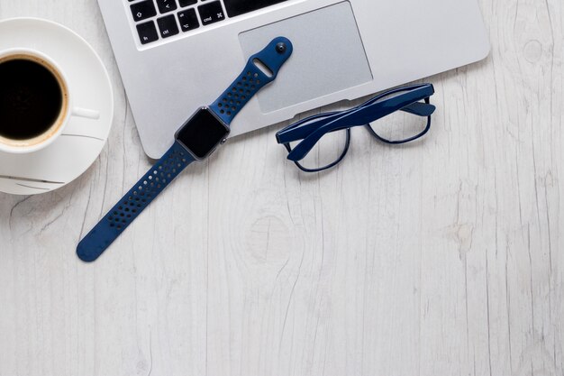 Glasses and watch near laptop and coffee