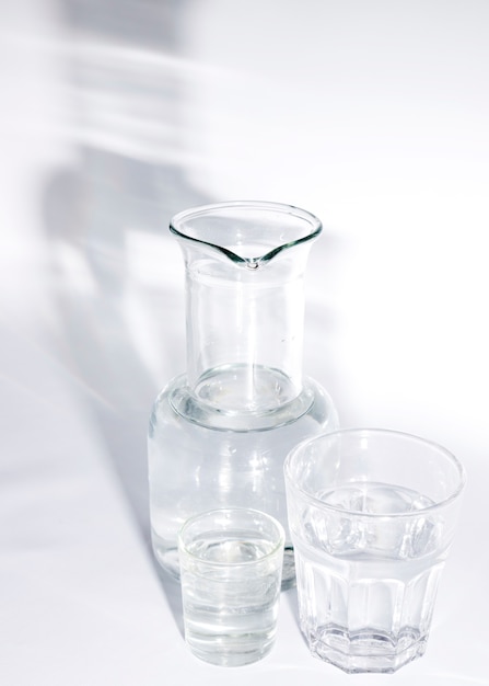 Glasses of water and beaker with shadow on white background