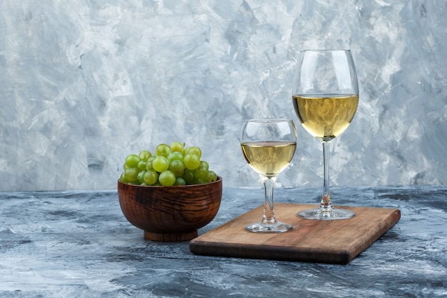 Free photo glasses of whisky on a cutting board with bowl of white grapes close-up on a dark and light blue marble background