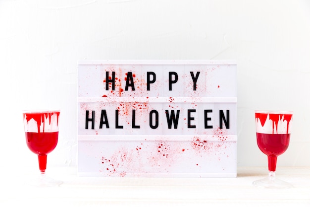 Glasses with fake blood near happy halloween writing