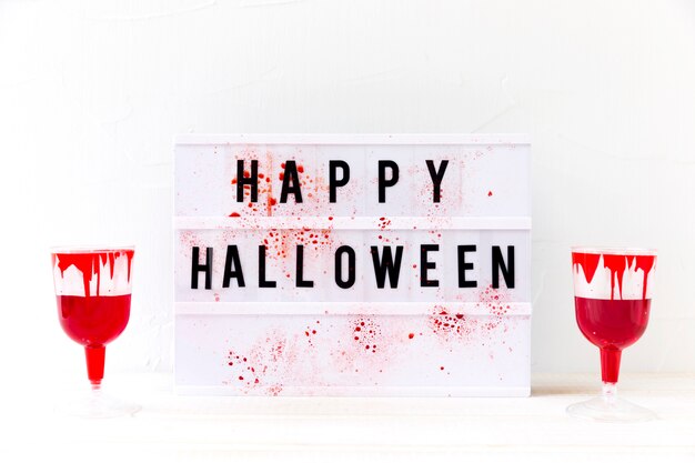 Glasses with fake blood near Happy Halloween writing