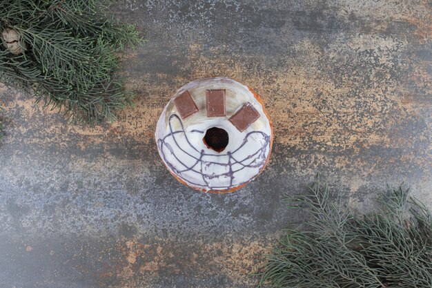 Glazed chocolate chip-topped donut between pine branches on marble surface