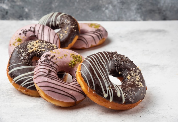 Glazed chocolate and pink donuts on marble surface.