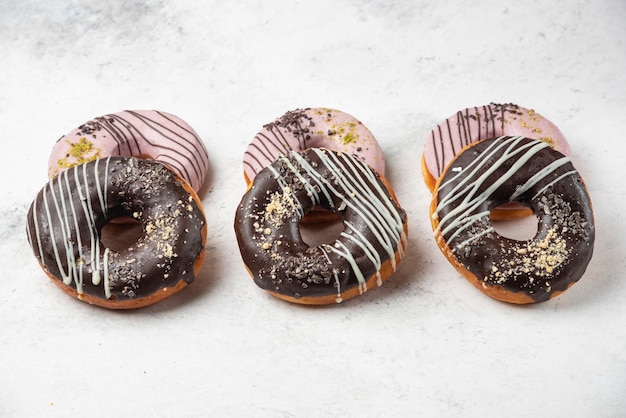 Foto gratuita cioccolato glassato e ciambelle rosa su superficie bianca.