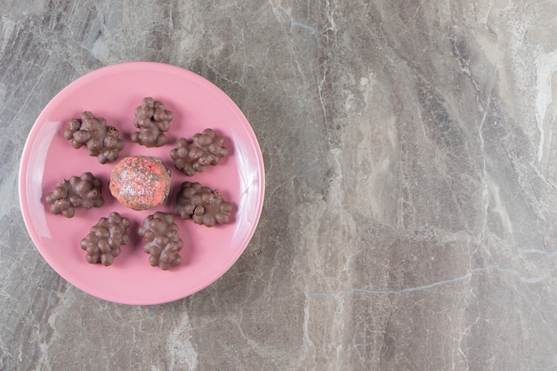 Glazed cookie and hazelnut chocolates on a plate on marble.